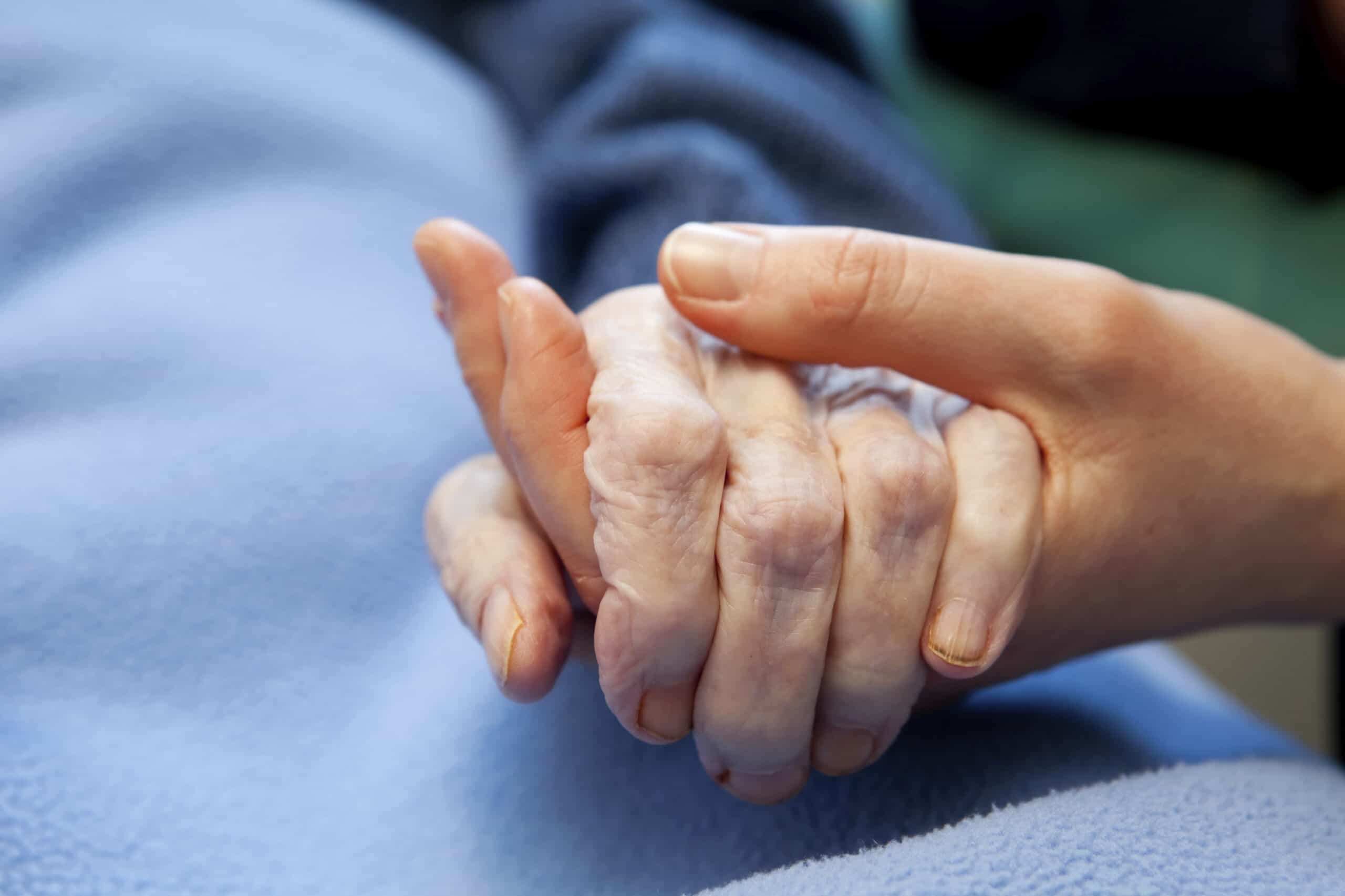 A caregiver holding a patient's hand during end of life care
