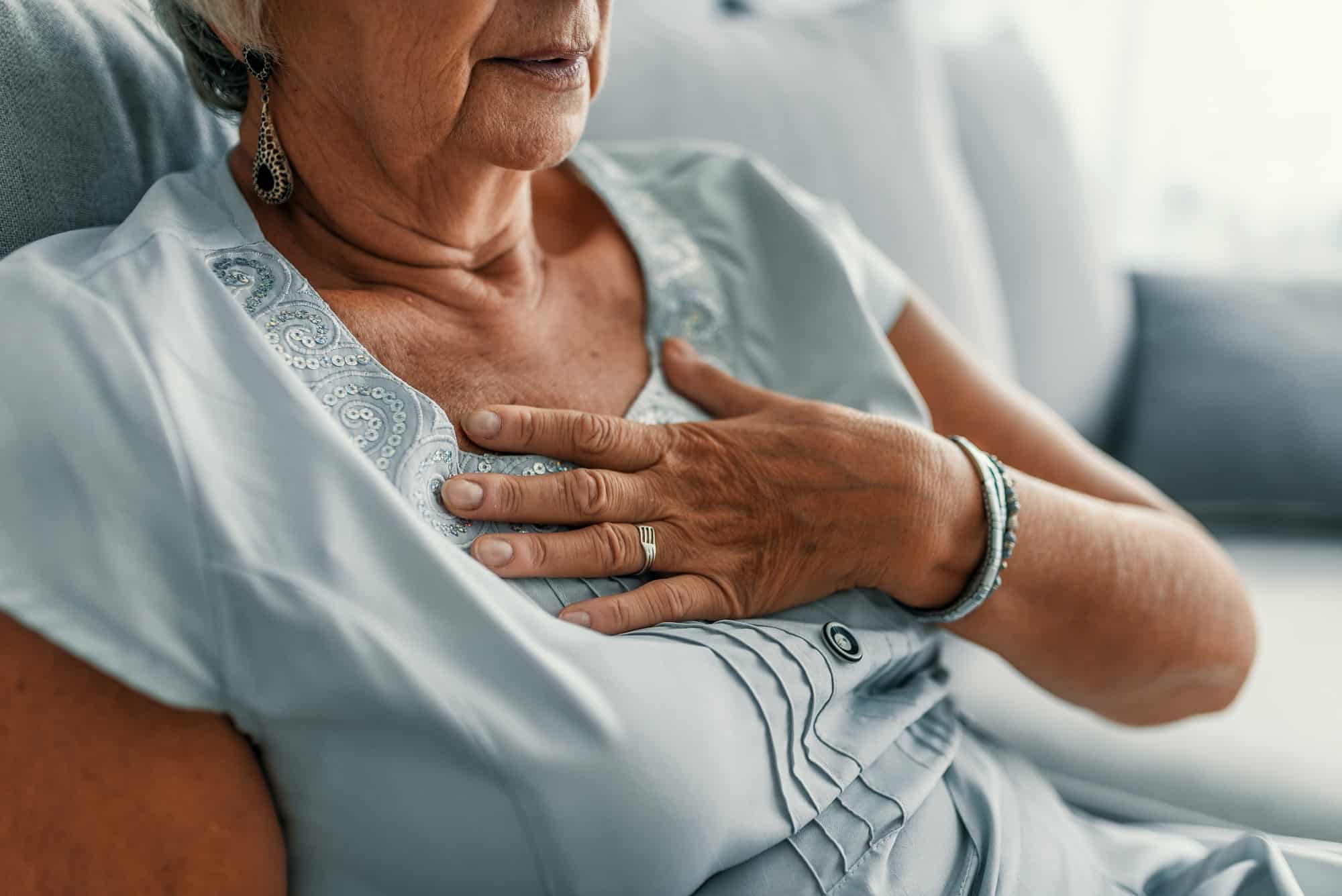 An older woman clutches her hand to her chest in pain