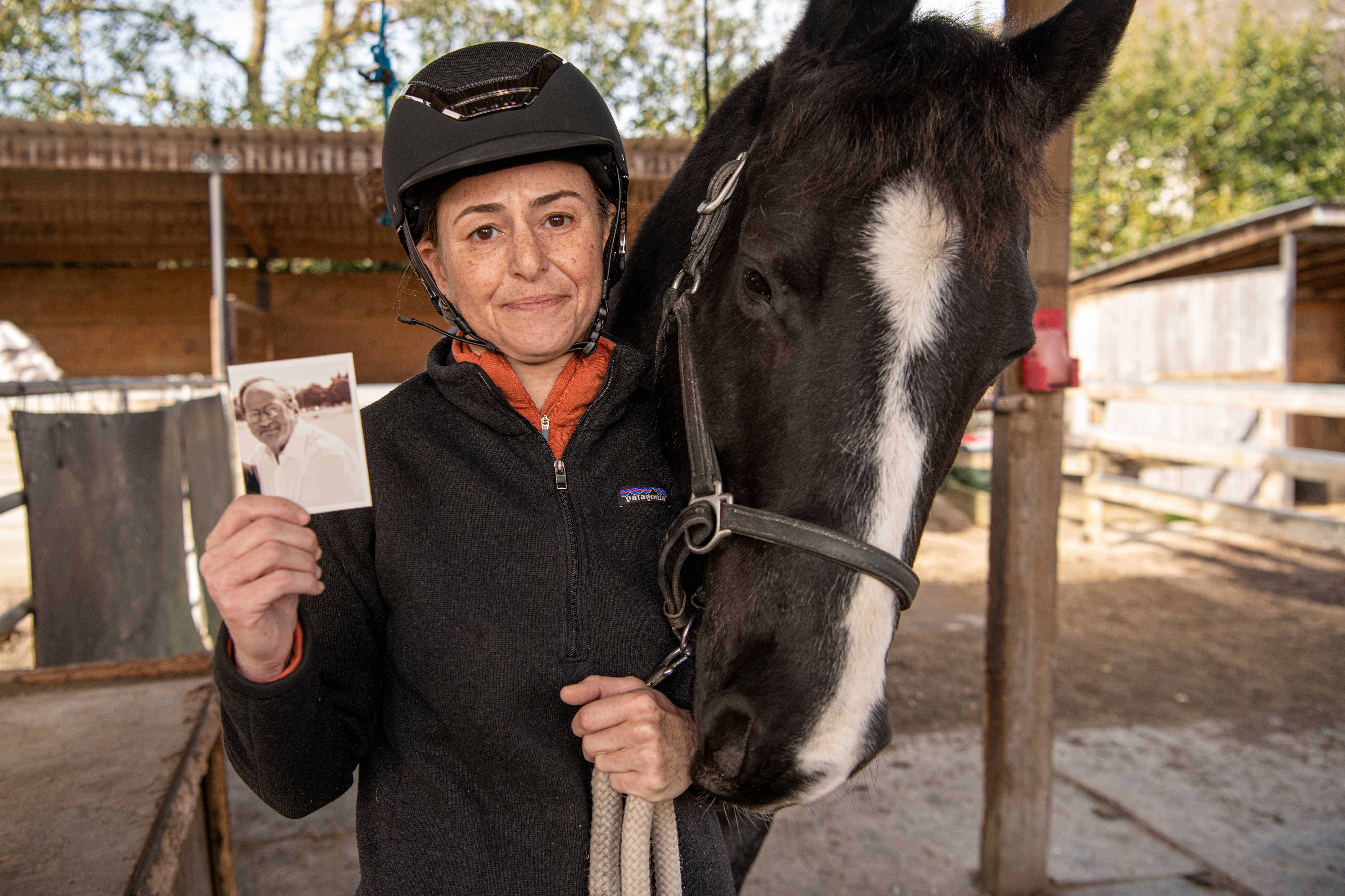 Woman smiling with her horse next to her while holding up a picture of her late father in her hand.