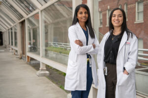 Two medical professionals who are both part of the Scotiabank Youth Transition Program standing side by side wearing white lab coats.