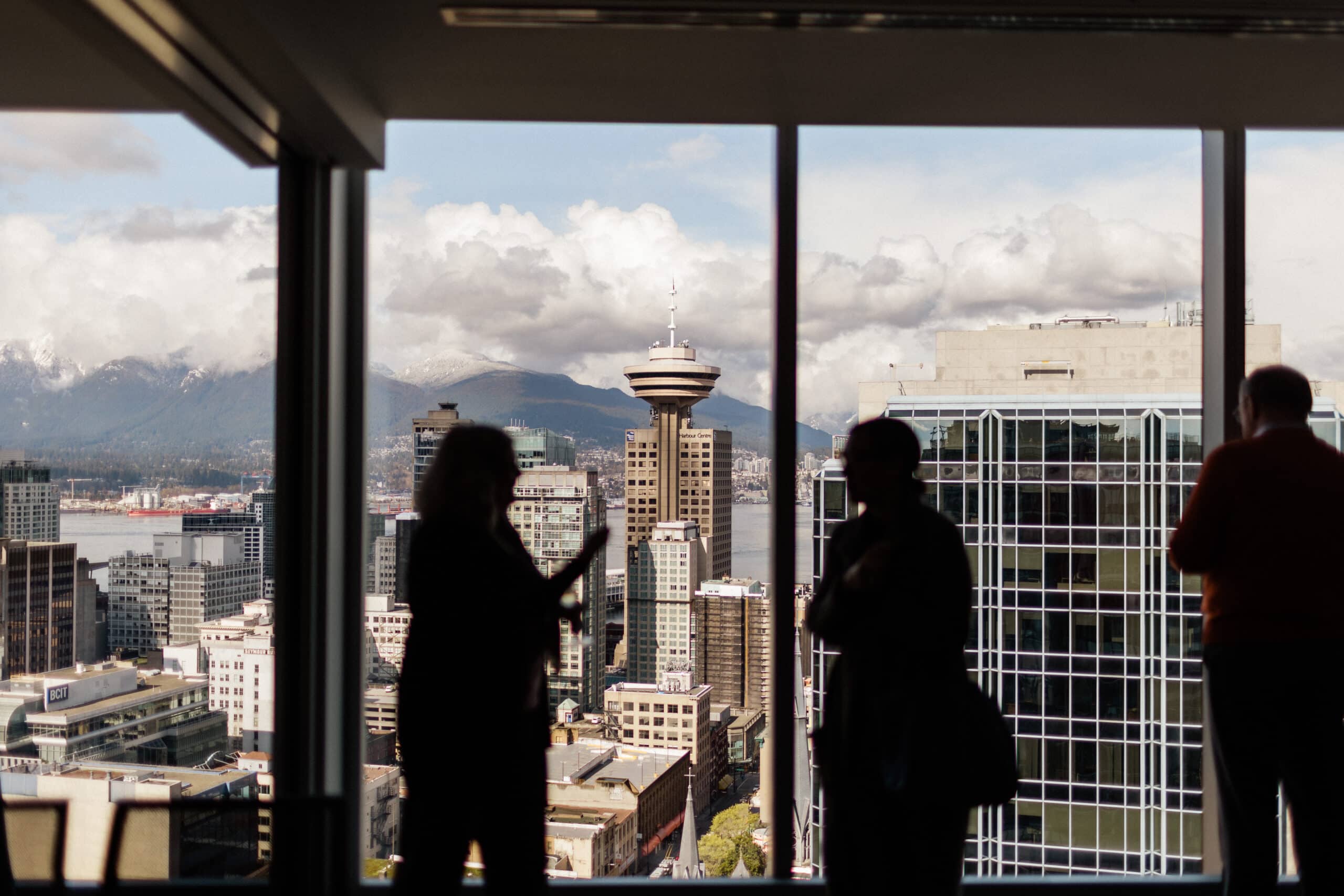 Silhouette of people standing in front of a window looking out at a view of downtown Vancouver skyline.