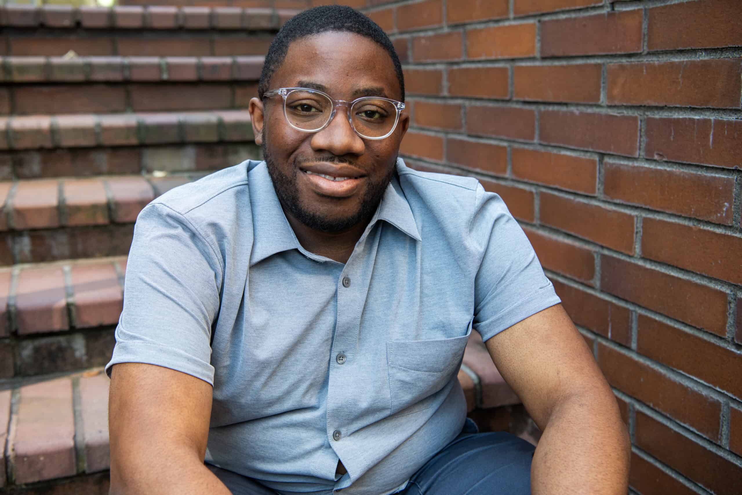 Dammy sits on stairs in front of a brick wall.