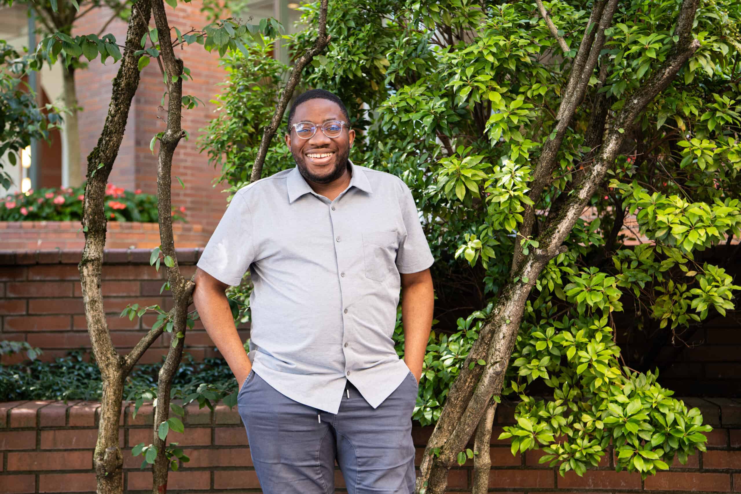 Dammy stands, smiling, in front of trees with greenery.