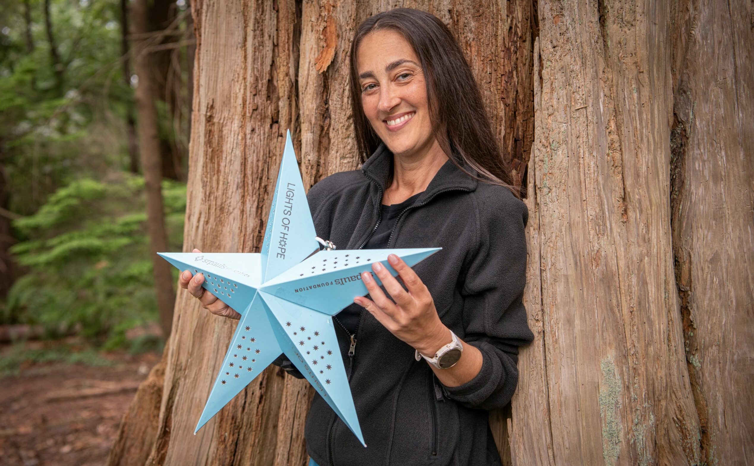 Karam, standing in front of a tree, holds a Lights of Hope lantern.