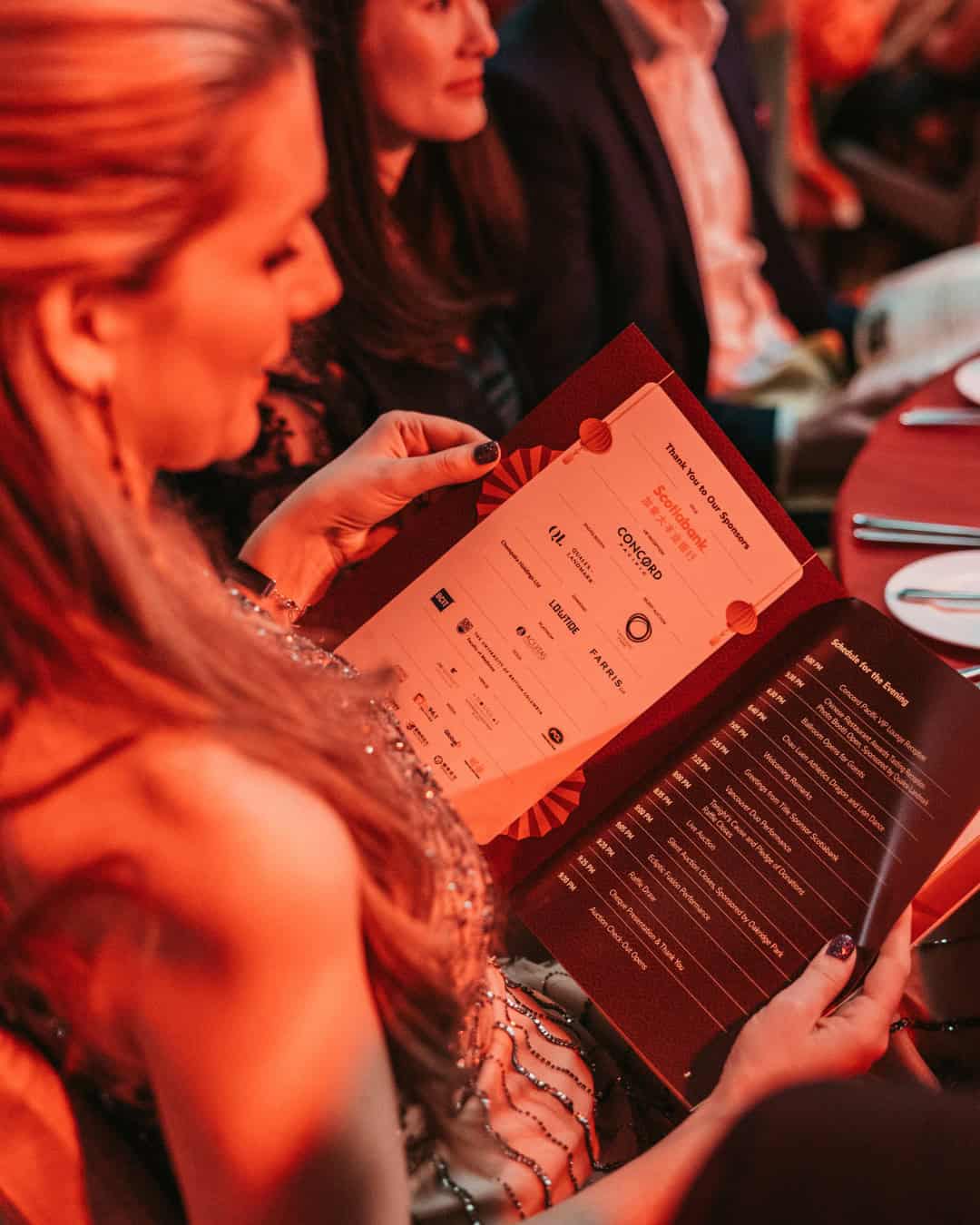 Photo of attendee at the 2024 Feast of Fortune gala holding the program guide with sponsor logos visible on page