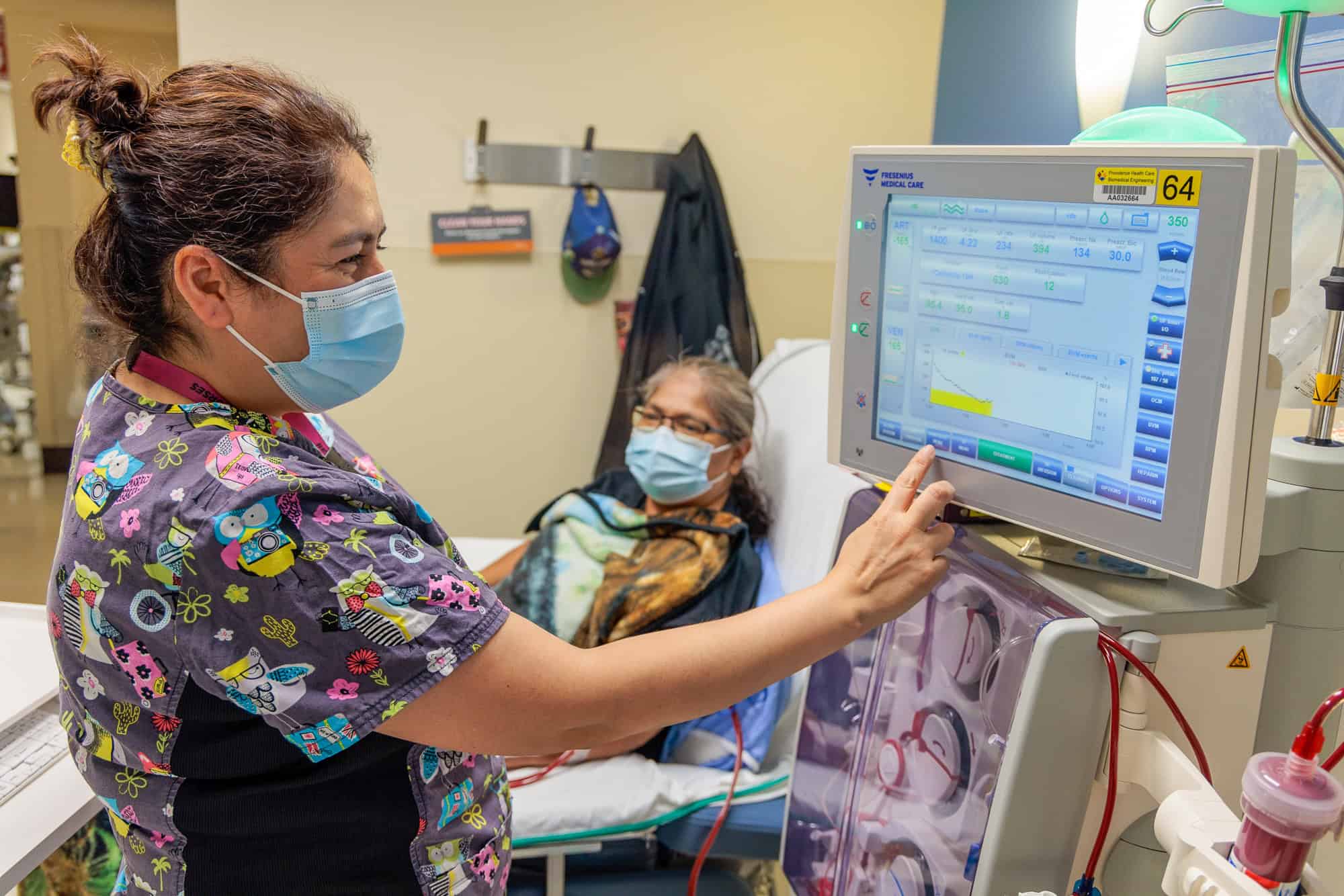 Patient in bed looking at a health care worker while getting a dialysis.