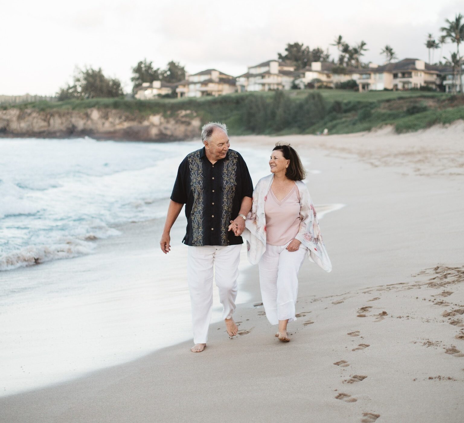 Brian and his wife Valerie walk down the beach, holding hands and smiling at each other.