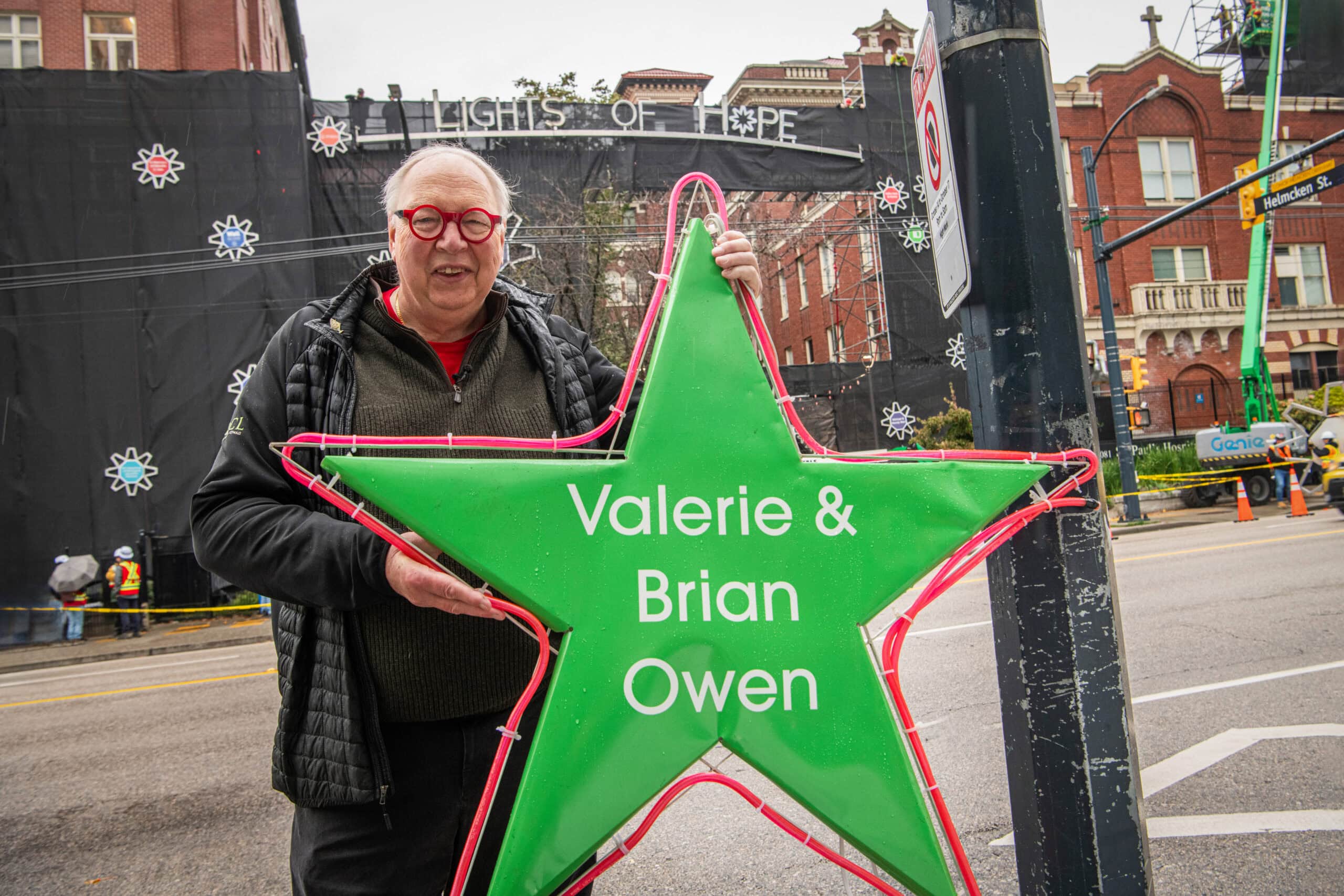 Brian stands holding a big green Lights of Hope star in front of St. Paul's Hospital.