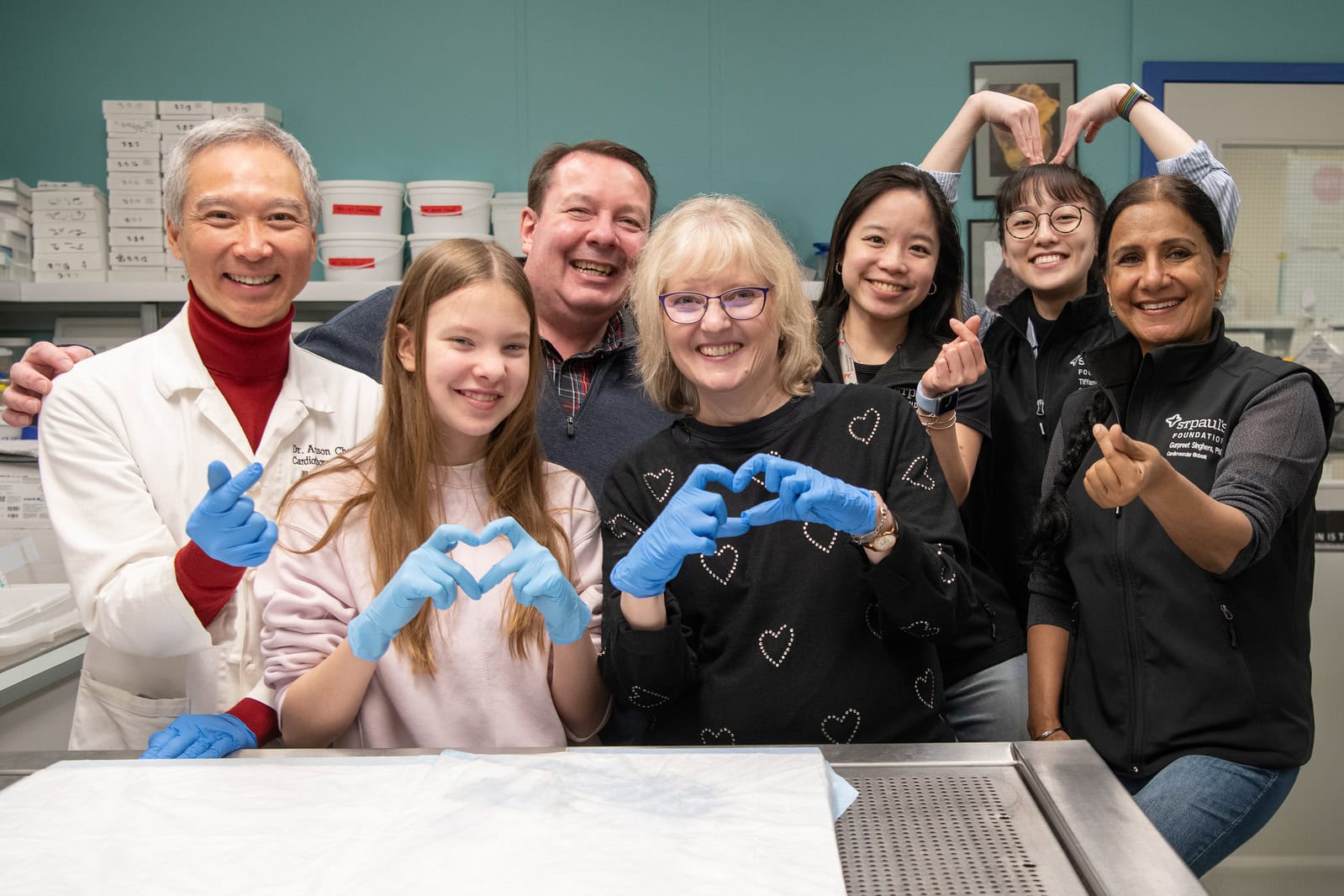 Heart transplant recipient Christine with her health care team at St. Paul's Hospital and her daughter and husband making heart with their hands.