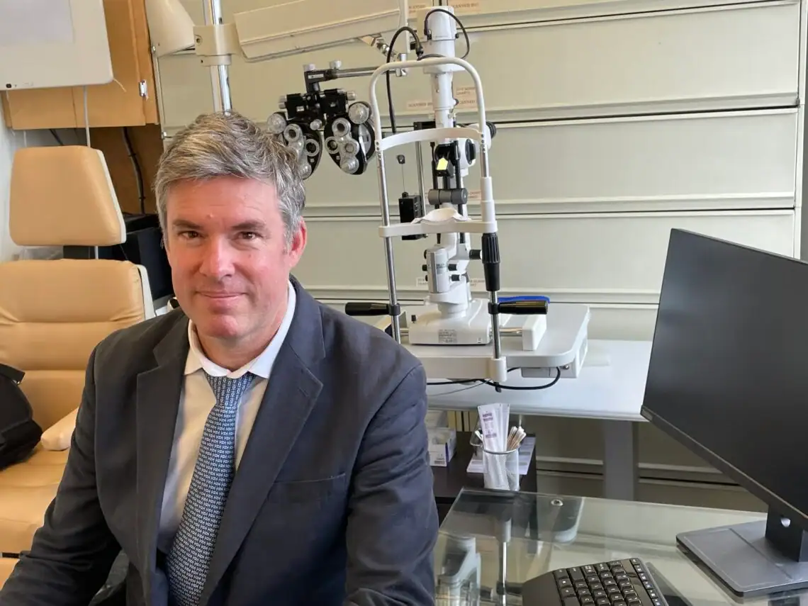 Dr. Moloney sits in his office in front of his ophthalmology equipment.